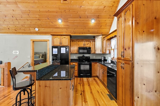 kitchen featuring sink, a breakfast bar, a center island, black appliances, and dark stone counters