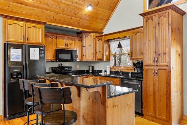 kitchen featuring vaulted ceiling, a breakfast bar area, dark stone counters, black appliances, and light hardwood / wood-style flooring