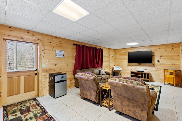 living room featuring light tile patterned flooring, a drop ceiling, and wooden walls