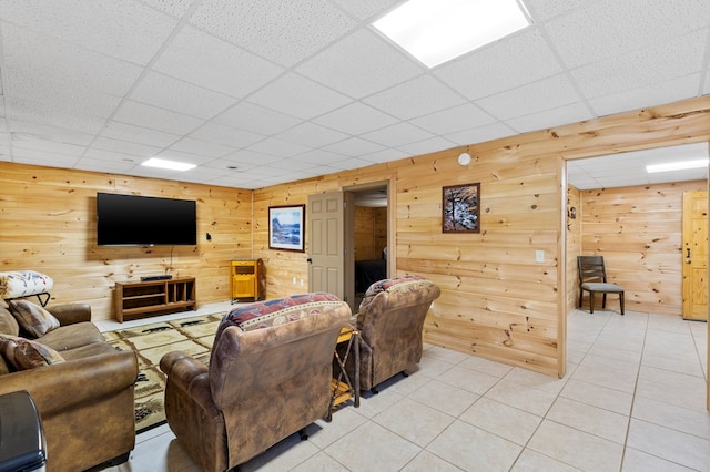 living room featuring a drop ceiling, wooden walls, and light tile patterned flooring