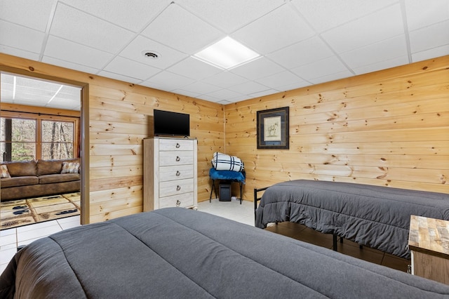 bedroom with a drop ceiling, wooden walls, and tile patterned floors