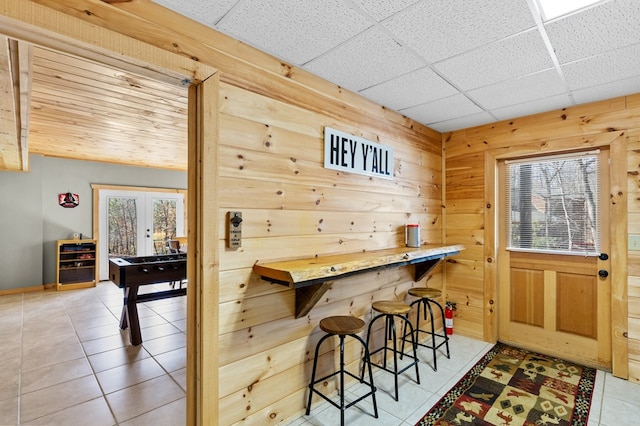 bar featuring french doors, a healthy amount of sunlight, tile patterned floors, and wood walls