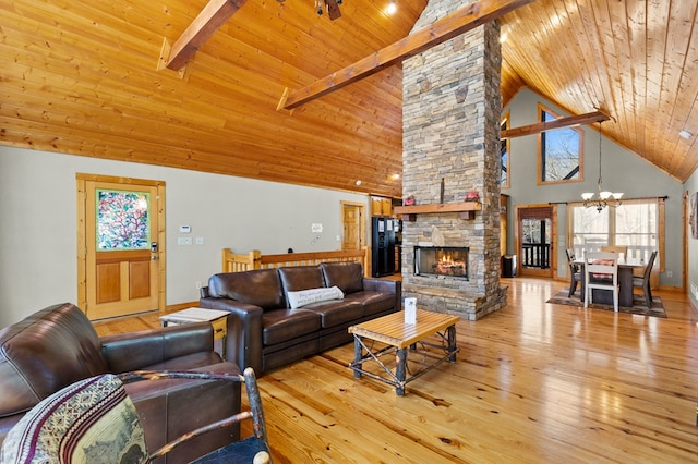 living room featuring beam ceiling, a notable chandelier, light hardwood / wood-style floors, a stone fireplace, and wooden ceiling