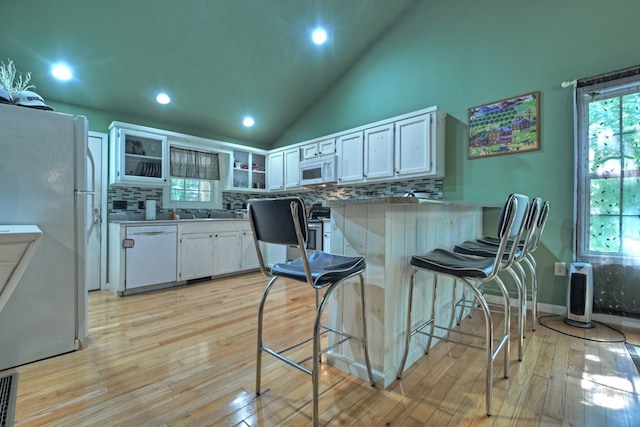 kitchen with white appliances, white cabinetry, light hardwood / wood-style floors, and a breakfast bar area