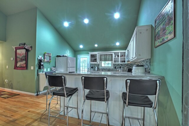 kitchen with white refrigerator, light hardwood / wood-style floors, kitchen peninsula, white cabinetry, and a kitchen bar