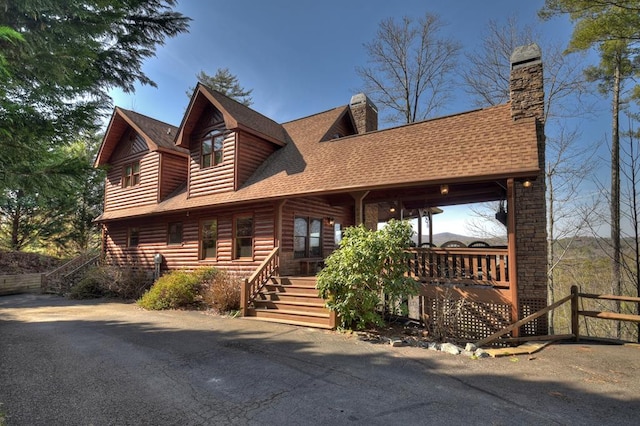 cabin with a shingled roof, faux log siding, a chimney, stairway, and a porch