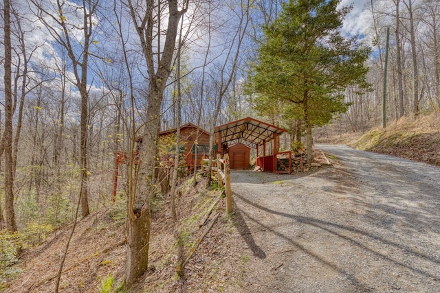 view of front of home featuring a detached carport, dirt driveway, an outbuilding, and a wooded view