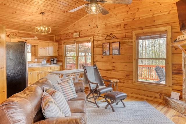 living area featuring light wood finished floors, wood walls, ceiling fan with notable chandelier, lofted ceiling, and wood ceiling