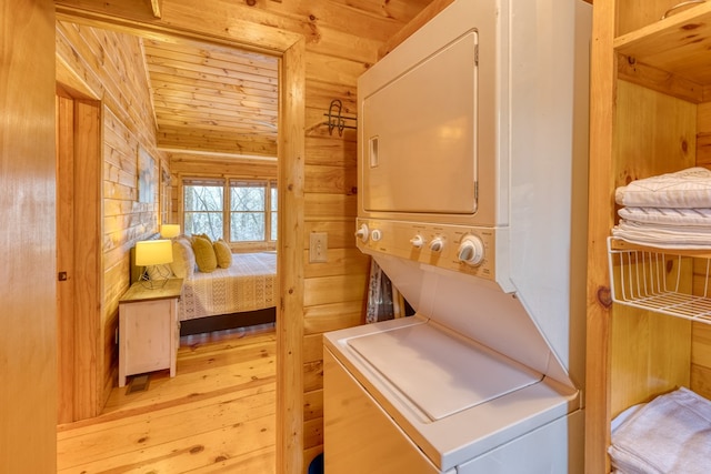 clothes washing area with wood ceiling, stacked washing maching and dryer, and wood finished floors