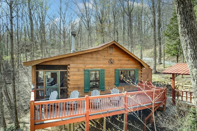 back of house with a view of trees, a wooden deck, and log siding