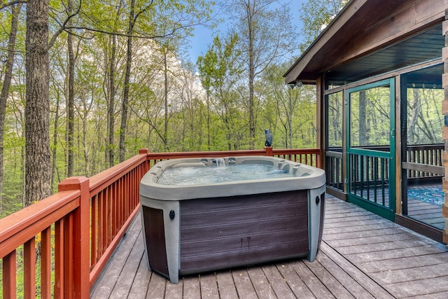 wooden deck featuring a sunroom, a view of trees, and a hot tub