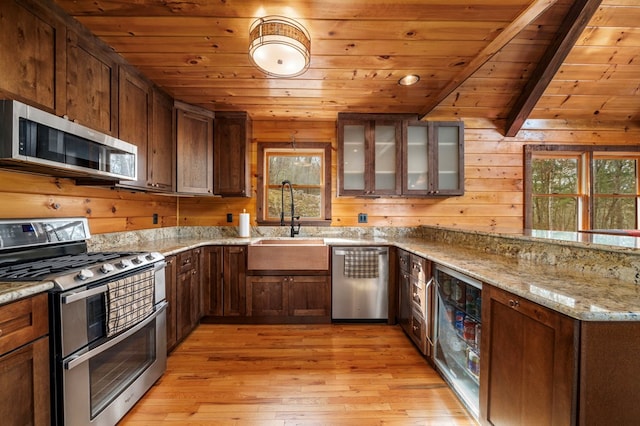 kitchen featuring wood walls, a wealth of natural light, lofted ceiling with beams, and appliances with stainless steel finishes