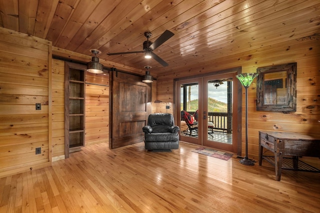 unfurnished room featuring wooden walls, light hardwood / wood-style flooring, ceiling fan, a barn door, and wood ceiling