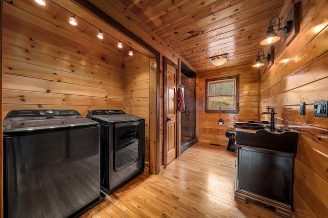 clothes washing area with separate washer and dryer, wooden walls, light hardwood / wood-style flooring, and wood ceiling