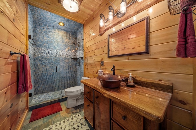 bathroom featuring vanity, wooden ceiling, wooden walls, toilet, and tiled shower