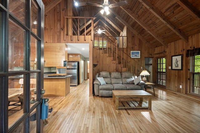 living area featuring wooden walls, high vaulted ceiling, light wood-style flooring, a ceiling fan, and wooden ceiling