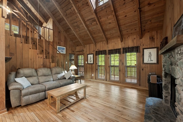 living room with wood ceiling, a stone fireplace, beamed ceiling, wooden walls, and light wood-style flooring