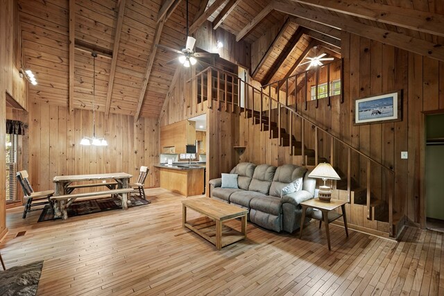 living room with wood-type flooring, wood walls, ceiling fan, and stairway