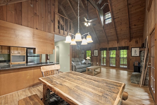dining area with beamed ceiling, wooden walls, high vaulted ceiling, light wood-type flooring, and wood ceiling