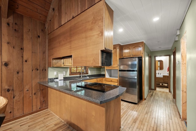 kitchen featuring freestanding refrigerator, a peninsula, light wood-style floors, a sink, and cooktop
