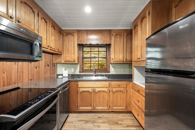 kitchen with a sink, appliances with stainless steel finishes, light wood-style floors, and brown cabinets