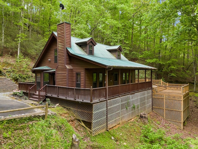 view of home's exterior featuring a wooden deck, a forest view, a chimney, and metal roof