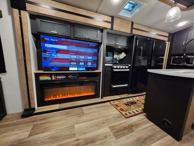 bar with light wood-style floors, a glass covered fireplace, freestanding refrigerator, and wall oven