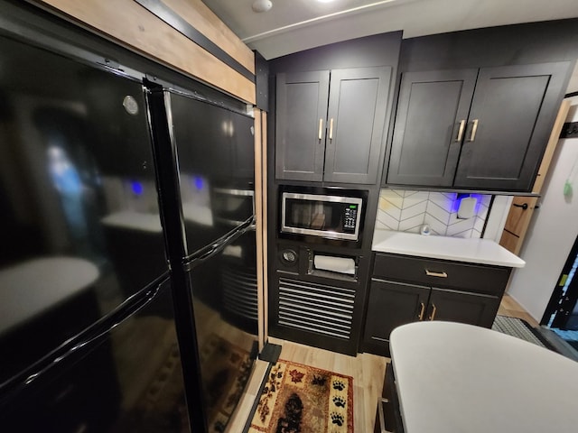 kitchen featuring light countertops, stainless steel microwave, freestanding refrigerator, dark cabinets, and light wood-type flooring