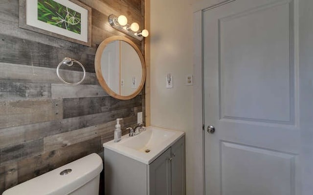 bathroom with toilet, vanity, and wood walls