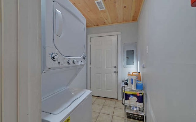 laundry area with wooden ceiling, light tile patterned floors, stacked washer and clothes dryer, and electric panel