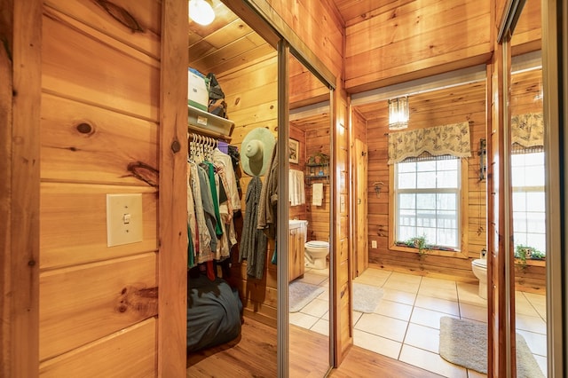 interior space featuring tile patterned floors, wood walls, toilet, and wood ceiling