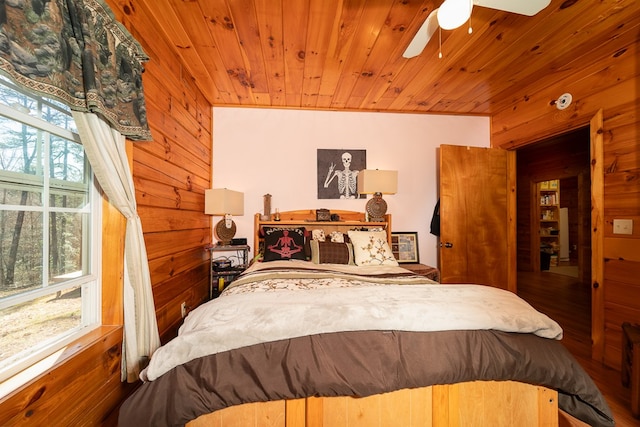 bedroom featuring wood walls, hardwood / wood-style flooring, multiple windows, and ceiling fan