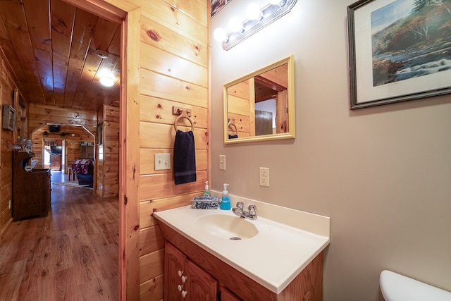 bathroom with wooden walls, vanity, wood-type flooring, wooden ceiling, and toilet