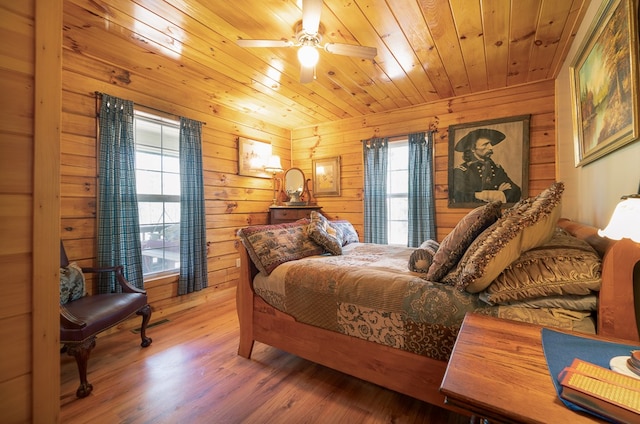 bedroom with wooden walls, hardwood / wood-style floors, multiple windows, and ceiling fan