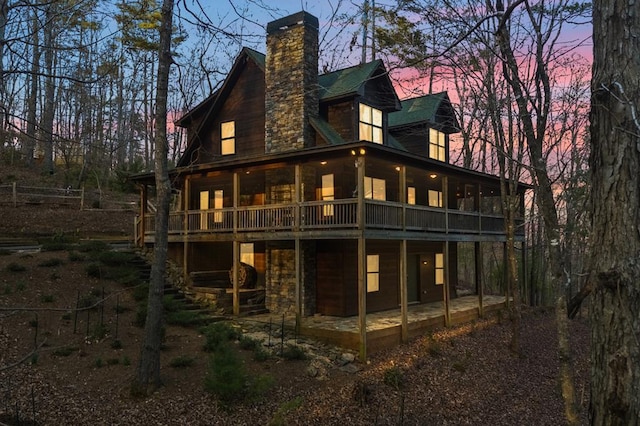 rear view of property with stone siding, a chimney, a patio, and a sunroom