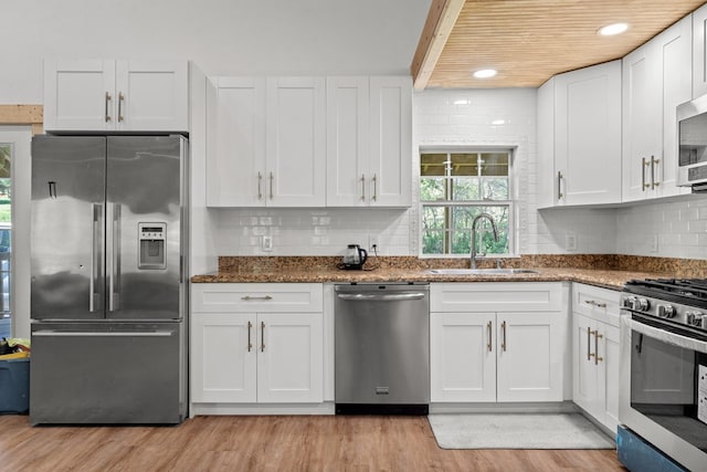 kitchen featuring a sink, light wood-type flooring, white cabinetry, backsplash, and appliances with stainless steel finishes