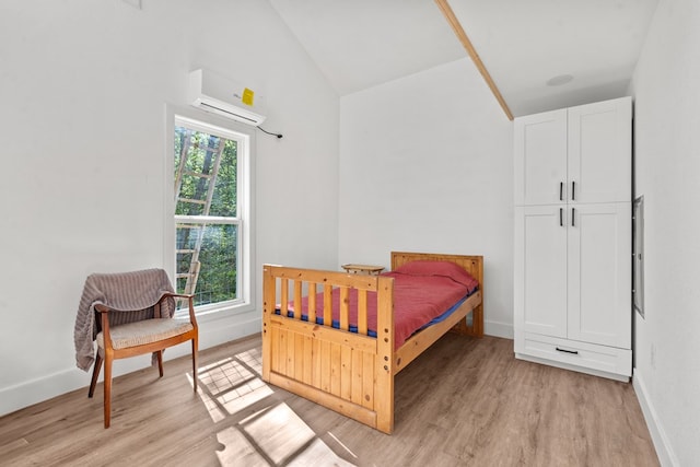 bedroom featuring high vaulted ceiling, an AC wall unit, baseboards, and light wood finished floors