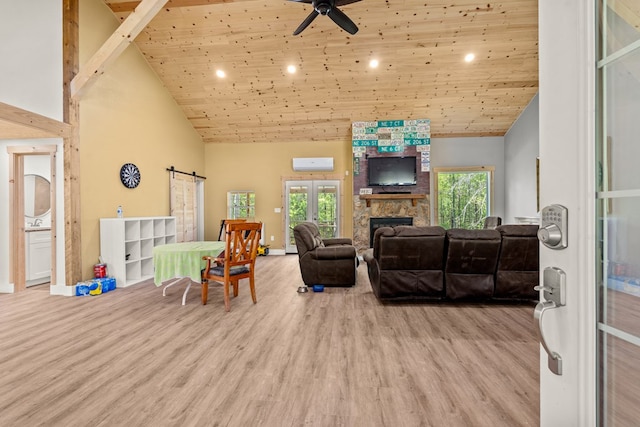 living area featuring a barn door, light wood-type flooring, recessed lighting, a stone fireplace, and high vaulted ceiling