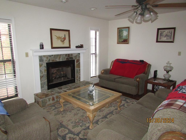 living room featuring ceiling fan and a stone fireplace