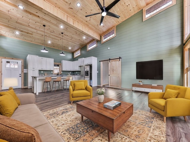 living room featuring ceiling fan, a barn door, hardwood / wood-style flooring, high vaulted ceiling, and beamed ceiling