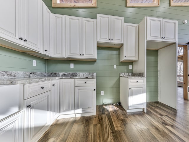 kitchen with light stone countertops, dark wood-type flooring, and wooden walls
