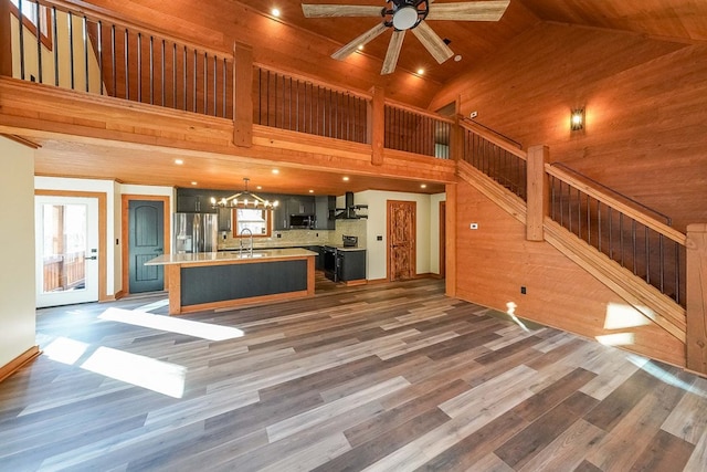 unfurnished living room featuring wooden walls, dark hardwood / wood-style flooring, sink, and high vaulted ceiling