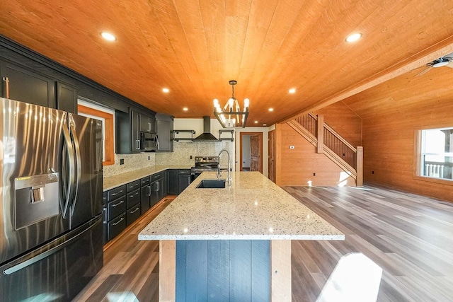 kitchen with dark wood-type flooring, wooden walls, a center island with sink, wood ceiling, and appliances with stainless steel finishes