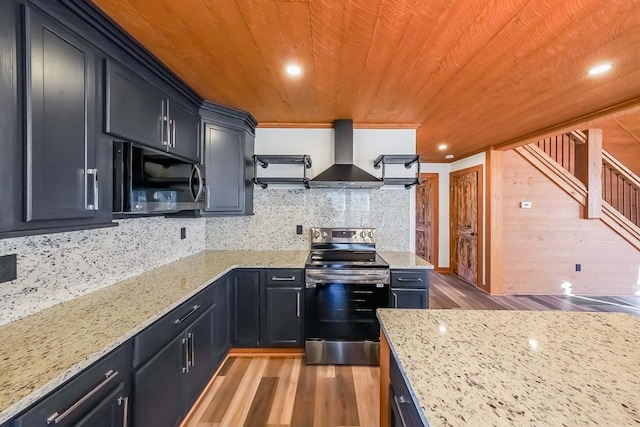 kitchen with light stone countertops, stainless steel appliances, wall chimney range hood, backsplash, and hardwood / wood-style flooring