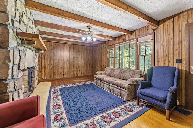 living room with a textured ceiling, hardwood / wood-style flooring, ceiling fan, and a stone fireplace