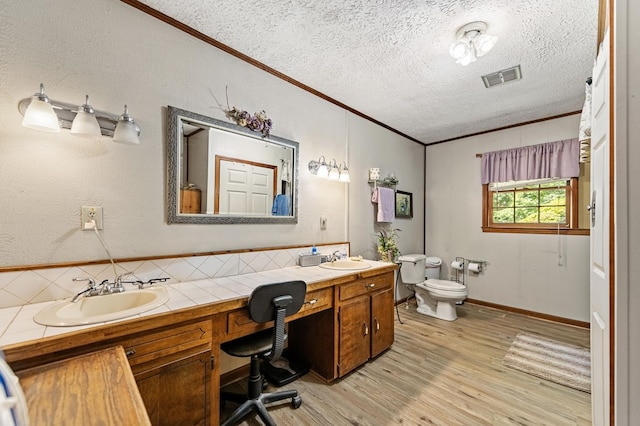 bathroom featuring a textured ceiling, hardwood / wood-style floors, toilet, vanity, and ornamental molding