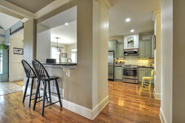 kitchen featuring a breakfast bar area, stainless steel appliances, green cabinetry, decorative light fixtures, and kitchen peninsula