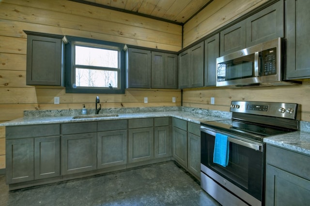 kitchen featuring light stone counters, sink, wooden walls, and stainless steel appliances