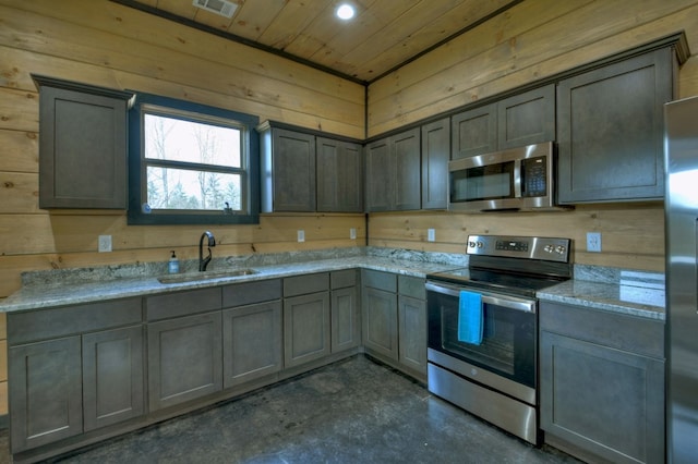 kitchen with light stone counters, appliances with stainless steel finishes, wooden walls, and sink