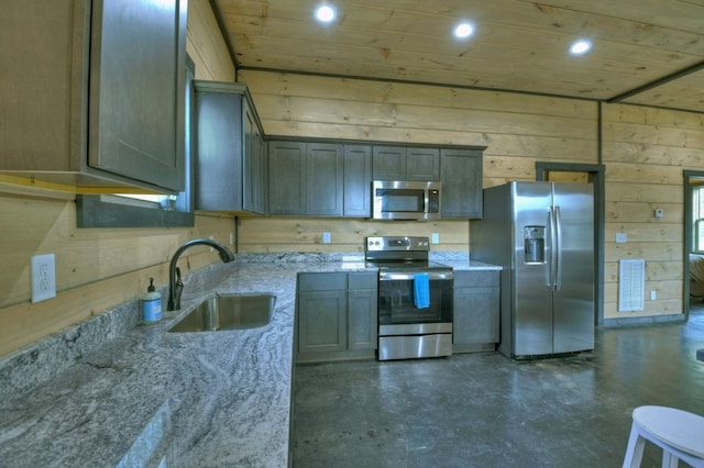 kitchen with sink, light stone counters, wooden ceiling, appliances with stainless steel finishes, and wooden walls